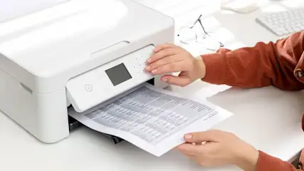 Hand bedient weißen Drucker; gedrucktes Blatt mit Tabellendaten wird herausgezogen.