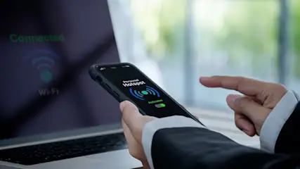 Hände halten Smartphone mit Personal Hotspot Aktivierung vor Laptop-Bildschirm.