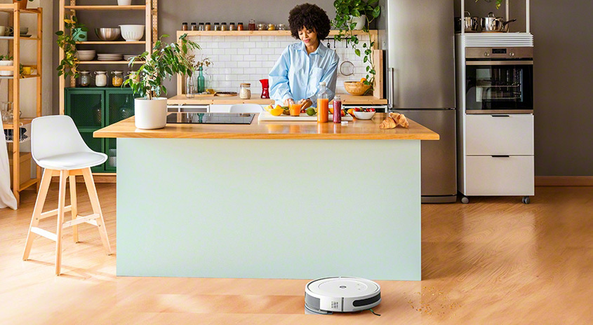 Eine Küche mit einer hellgrünen Kücheninsel mit Holzplatte und einem Staubsaugerroboter auf dem Holzboden.