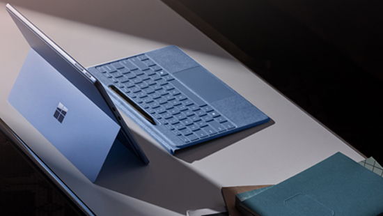 Blauer Laptop auf einem hellen Tisch, teilweise geöffnet, mit Stift auf der Tastatur. Im Hintergrund ein dunkler Bereich.