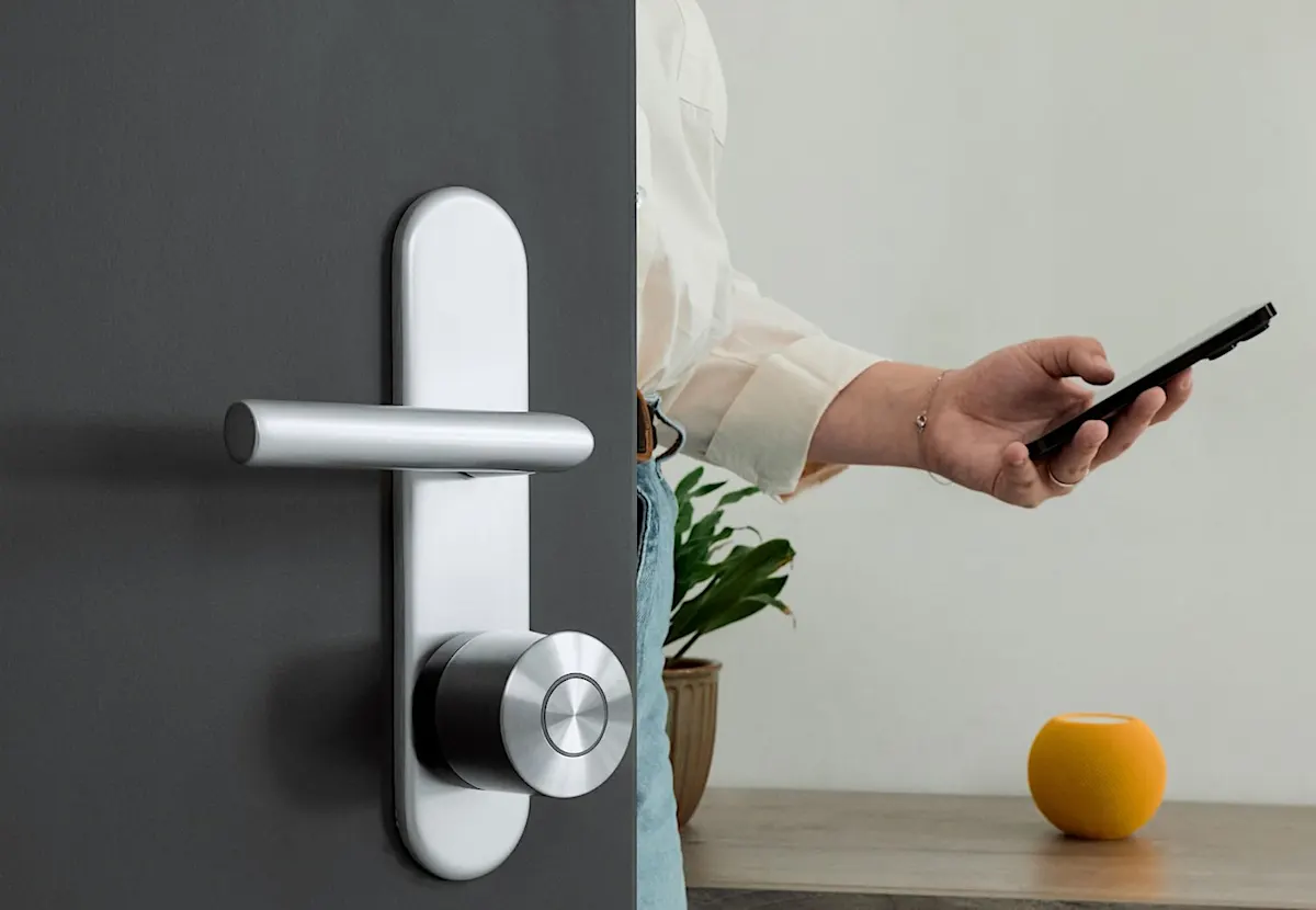Eine Person mit einem Smartphone in der Hand geht durch eine geöffnete dunkle Tür, auf der das Nuki Smart Lock Ultra montiert ist.