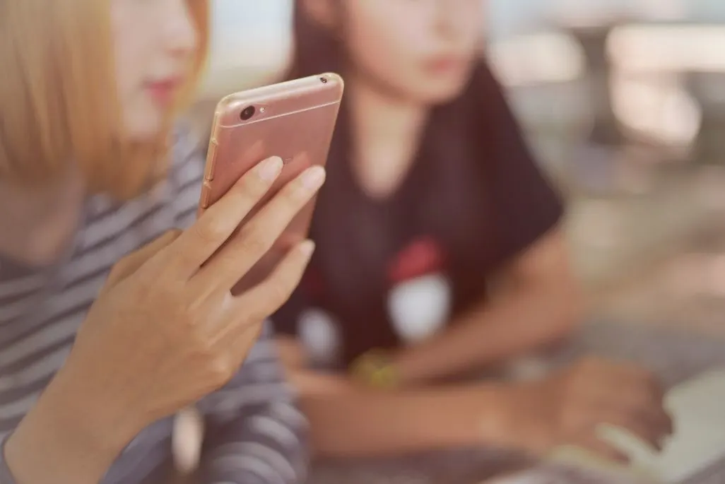 Zwei Personen sitzen nebeneinander, eine Person hält ein rosa Smartphone in der Hand