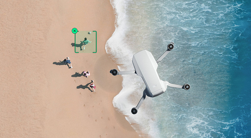 Weiße Drohne über Sandstrand und blauem Wasser. Einige Personen sind am Ufer zu sehen.