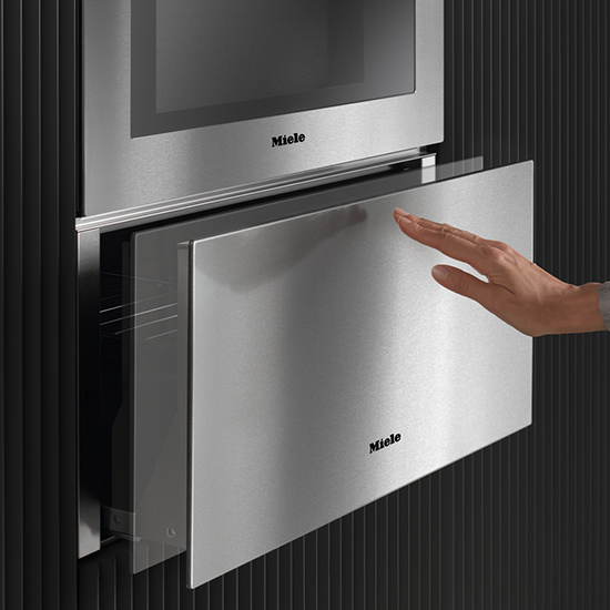 Nahaufnahme eines Miele-Edelstahlbackofens mit einer Hand, die eine Schublade öffnet.