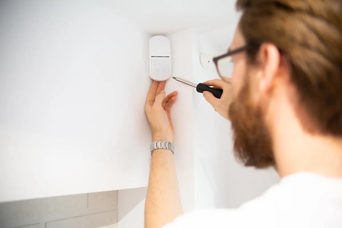 Mann montiert mit einem Schraubenzieher einen Bewegungsmelder an der Wand.