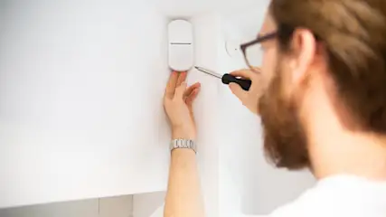 Mann montiert mit einem Schraubenzieher einen Bewegungsmelder an der Wand.