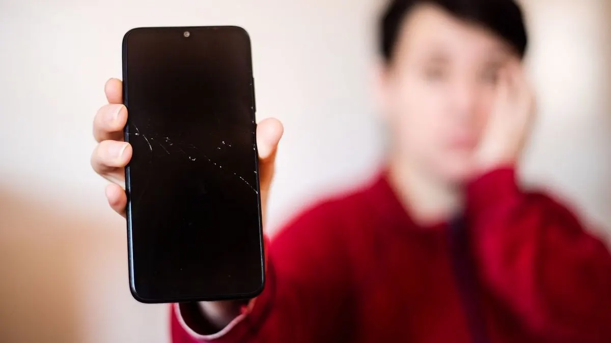 Eine Person hält ein Smartphone mit gesprungenem Display in die Kamera.