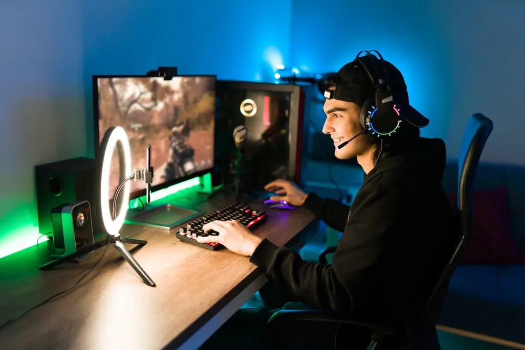 Gamer mit Headset streamt am beleuchteten Gaming-Setup bestehend aus zwei Monitoren und Ringlicht.