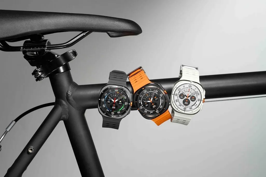 Drei Smartwatches mit verschiedenfarbigen Armbaendern haengen am Rahmen eines Fahrrads