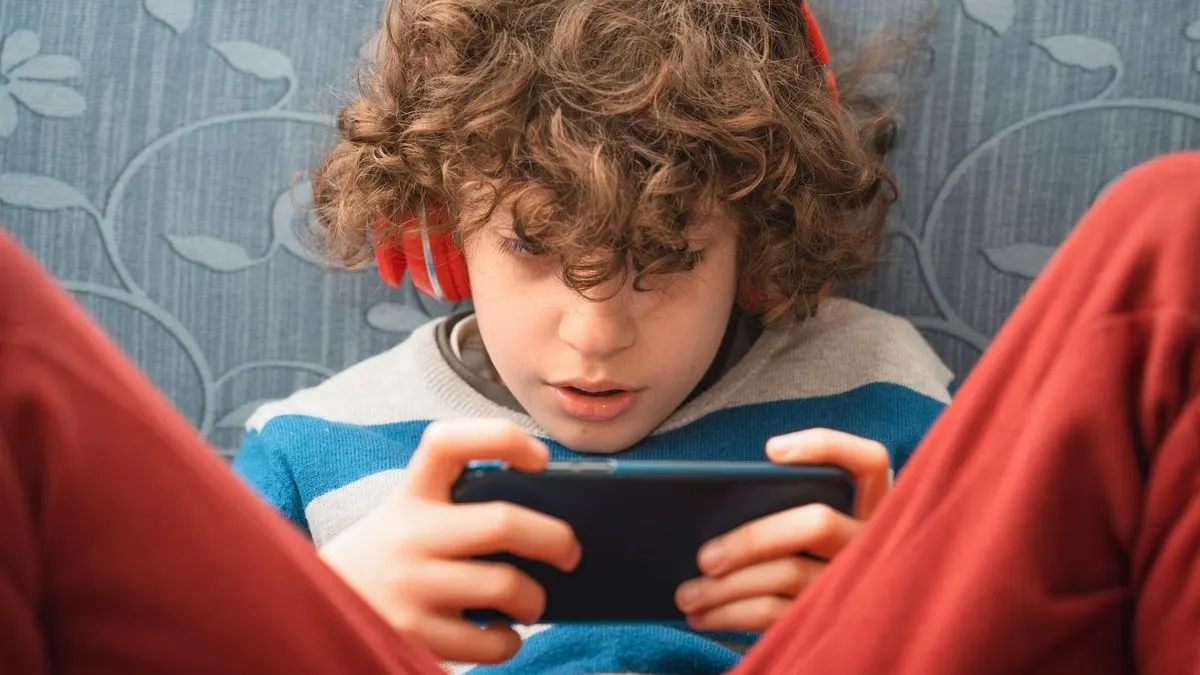 Kind sitzt auf Sofa und spielt mit einem Smartphone während es Kopfhörer trägt