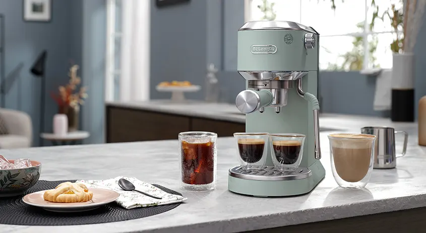 Eine mintgrüne Kaffeemaschine steht auf einer Küchentheke mit Getränken und Gebäck.