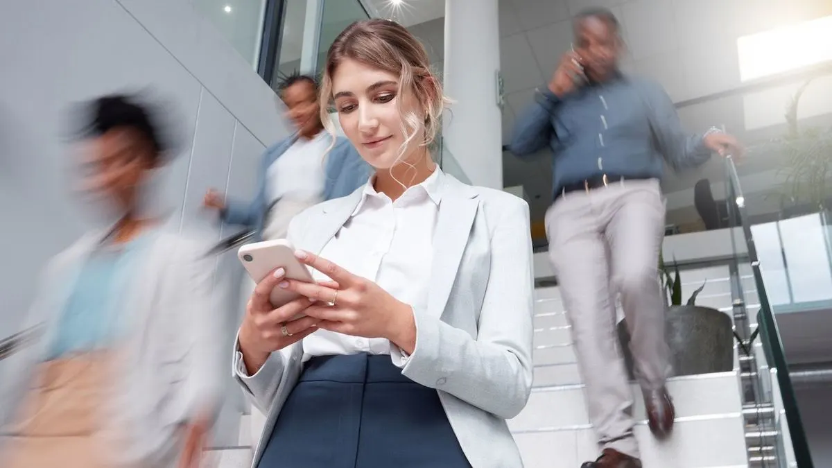 Frau im Business Outfit nutzt Smartphone auf einer Treppe im Büro.