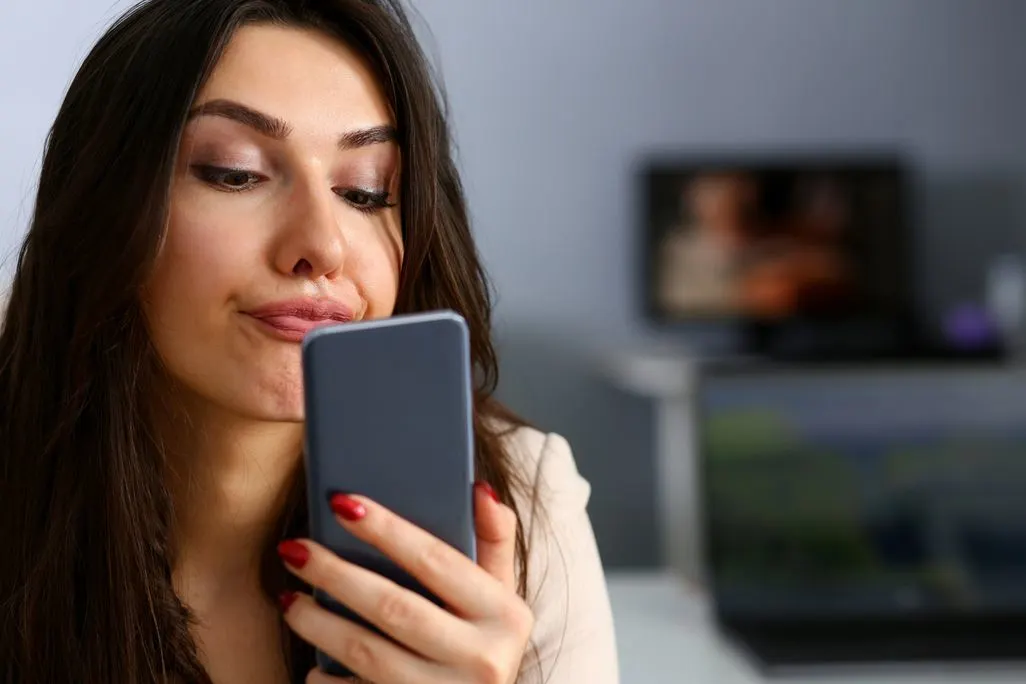 Dunkelhaarige Frau blickt genervt auf ihr Smartphone.