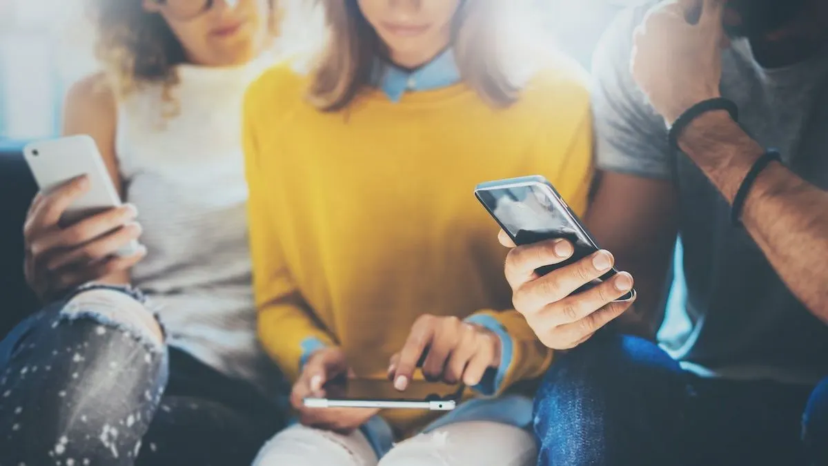 Drei Menschen sitzen zusammen und benutzen Smartphone und Tablet.