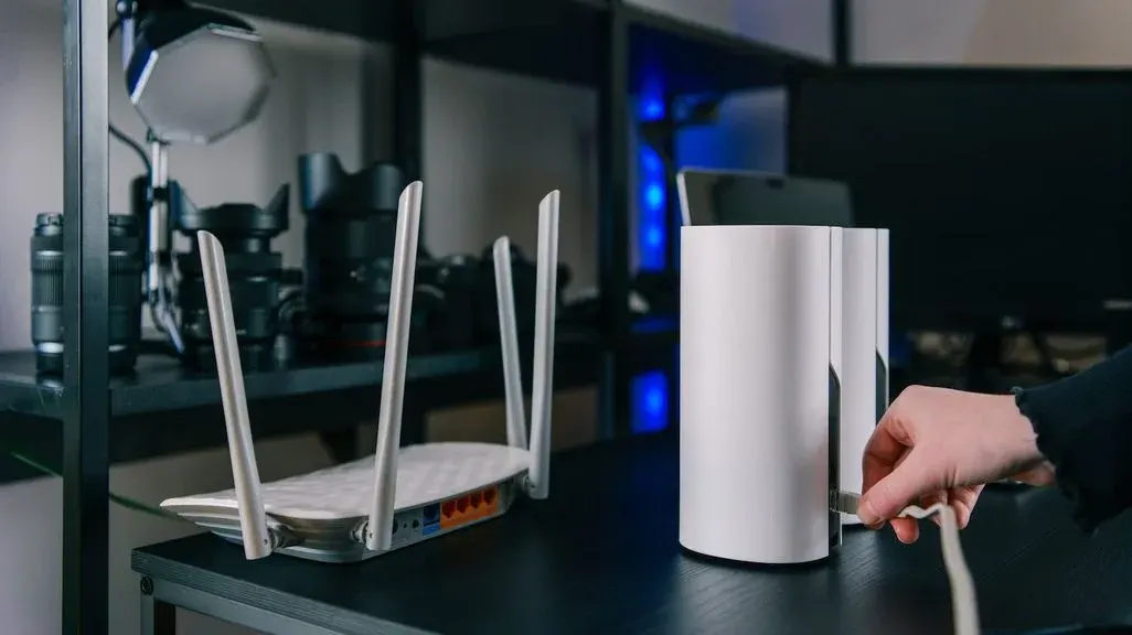 Hand hält weißen WLAN-Router neben einem anderen Router mit drei Antennen auf schwarzem Tisch in modernem Tech-Setup.