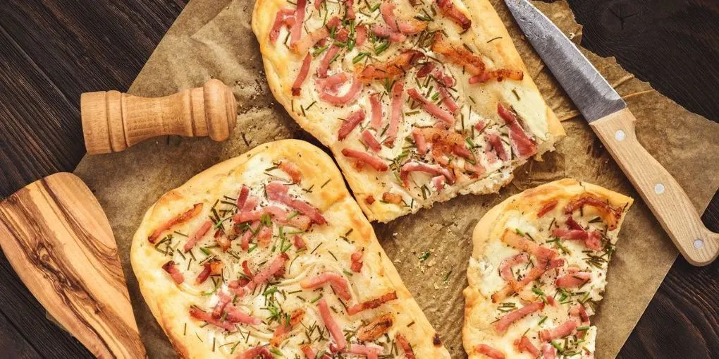 Klassischer Flammkuchen mit Speck und Schnittlauch auf Holzbrett angerichtet