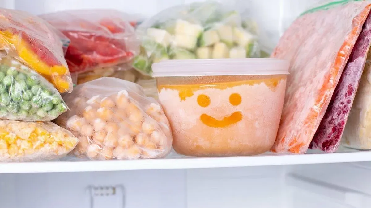 Ein Gefrierfach voller Gefrierbeutel mit gefrorenem Gemüse, Hülsenfrüchten und Obst. Ein orangefarbener Behälter zeigt ein Smiley-Gesicht.