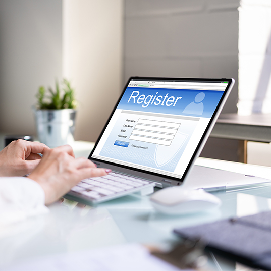 Eine Person tippt auf einem Laptop. Auf dem Bildschirm befindet sich eine Registrierungsseite mit Feldern zum Ausfüllen.