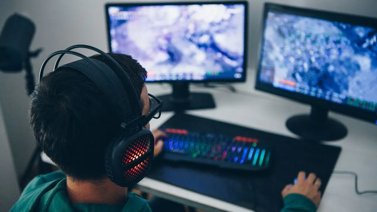 Ein Gamer mit beleuchteten Kophörern sitzt vor zwei Monitoren und tippt auf einer RGB-Tastatur