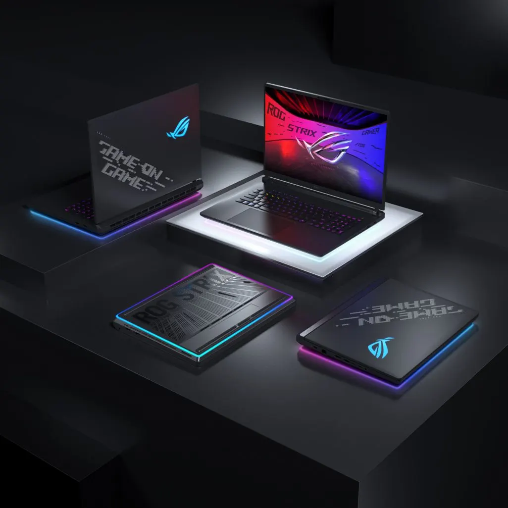 Vier ASUS ROG Strix Gaming-Laptops mit bunter RGB-Beleuchtung auf einer dunklen Fläche.