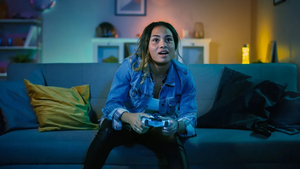 Person sitzt auf einem Sofa und spielt mit einem Gamecontroller ein Videospiel