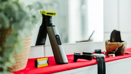 Ein elektrischer Rasierer steht aufrecht vor einem Spiegel umgeben von Zubehör.