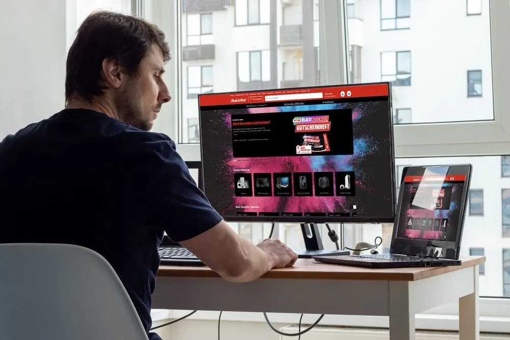 Mann betrachtet MediaMarkt-Website an externem Monitor und Laptop.