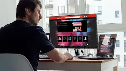 Mann betrachtet MediaMarkt-Website an externem Monitor und Laptop.