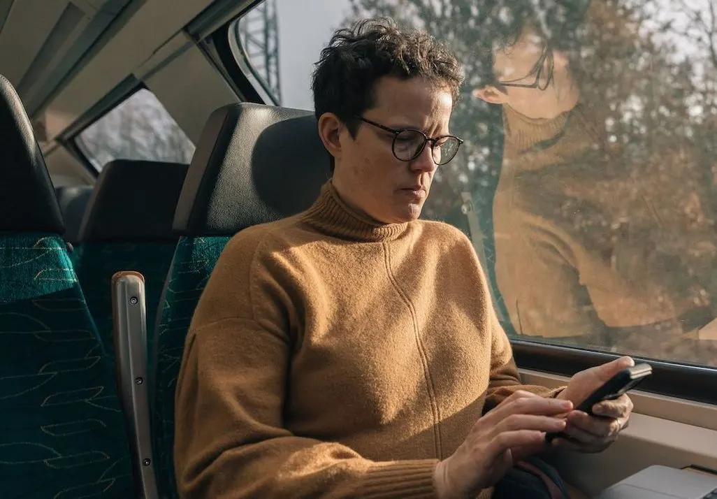 Mann mit braunem Pullover nutzt Smartphone in einem Zug.