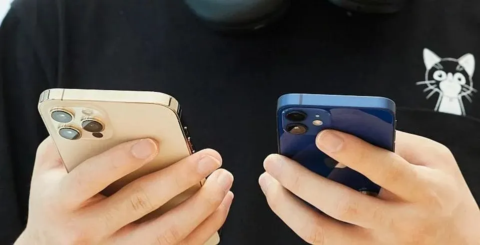 Eine Person hält ein großes goldenes und ein kleineres blaues iPhone.