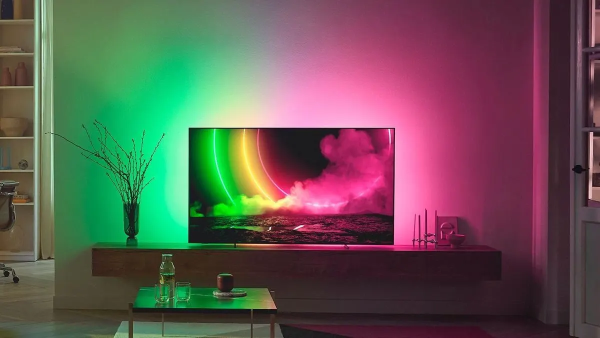 Fernseher mit gruen-pinkem Ambilight steht auf einem Holzregal