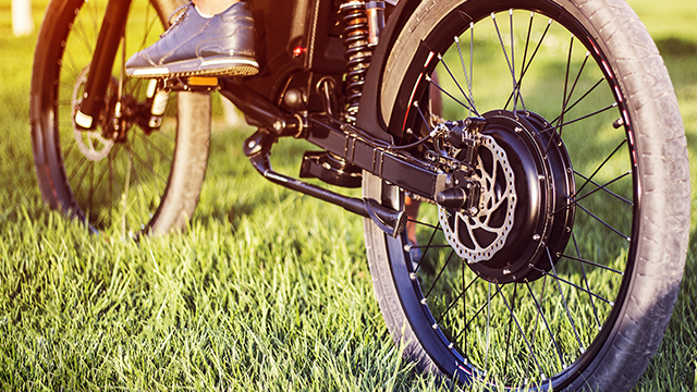 Nahaufnahme eines Fahrrads auf Gras. Der Fokus liegt auf dem Hinterrad mit Bremsscheibe und Elektroantrieb.