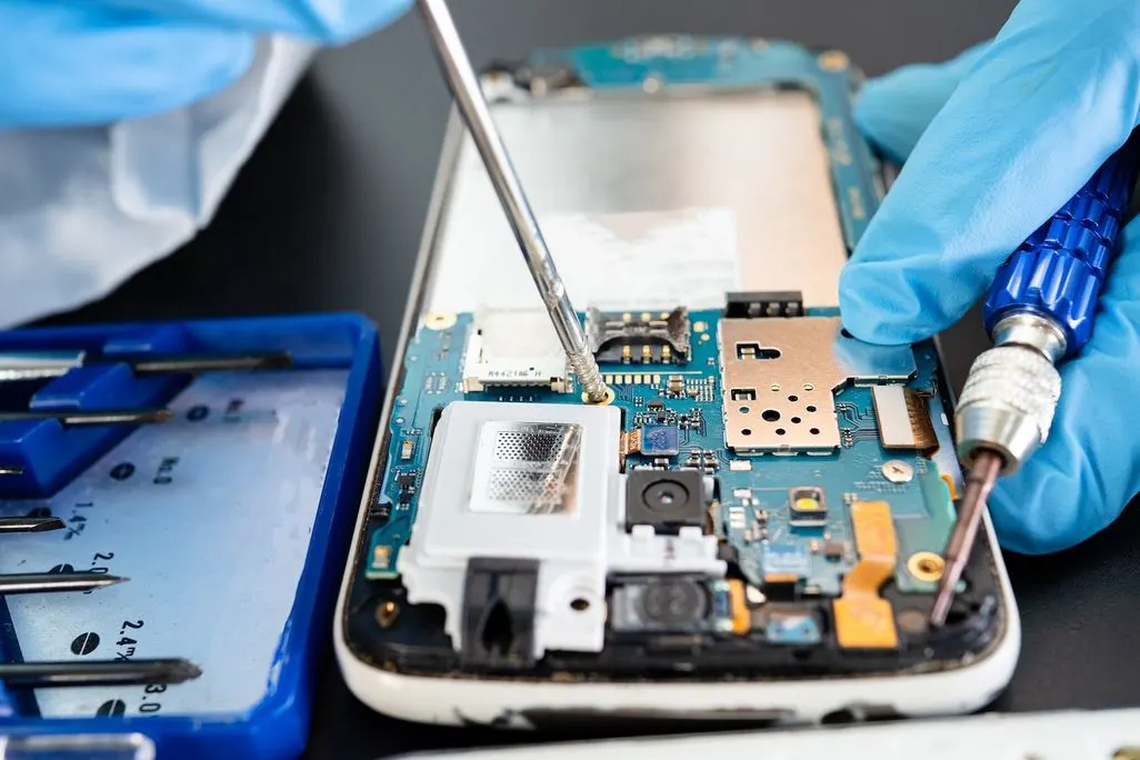 Ein Smartphone wird mit Werkzeug und Handschuhen repariert.