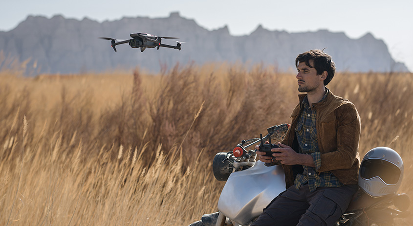 Ein Drohnenflug über einer trockenen Graslandschaft mit einem Motorrad und einem Helm im Vordergrund.