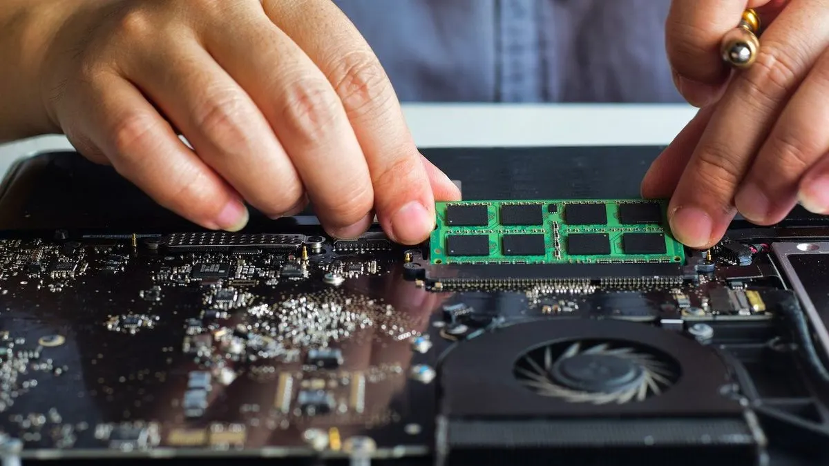 Haende setzen RAM-Speicher in geoeffneten Laptop ein, Mainboard und Luefter sind sichtbar