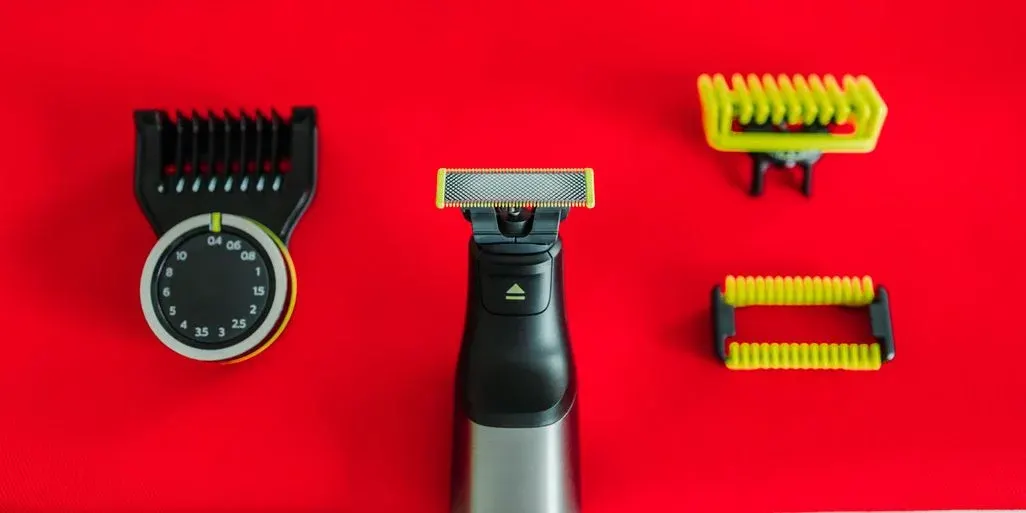  Elektrische Haarschneidemaschine mit schwarzem Aufsatz, Tiefenregler, Metallfolienklinge und zwei gelb-schwarzen Wechselaufsätzen auf rotem Hintergrund.