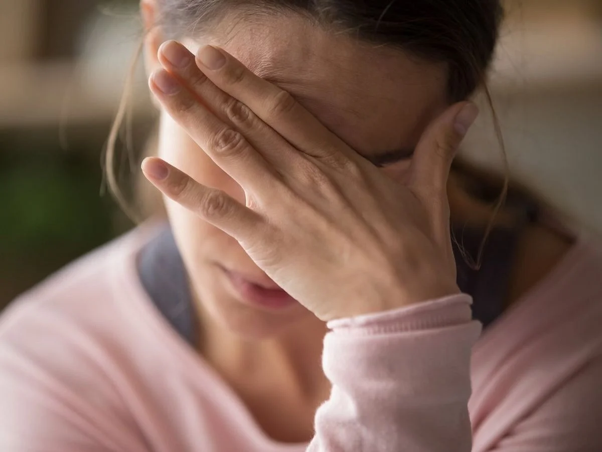 Frau greift sich mit Hand auf die Stirn