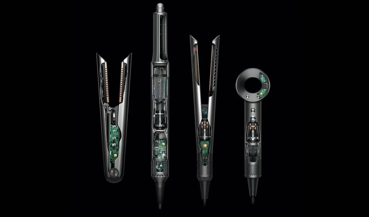 Vier Dyson-Styler und -Heißluftfön-Modelle in Schwarz und Silber mit sichtbarer Elektronik und internen Komponenten auf schwarzem Hintergrund – darunter zwei Lockenstäbe mit Gleitaufsätzen, ein vertikaler Heißluftfön und ein kompaktes Handgerät mit digitalem Display.