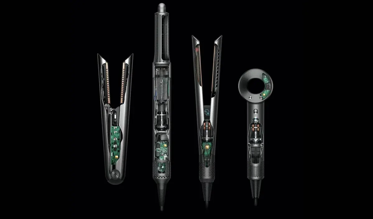 Vier Dyson-Styler und -Heißluftfön-Modelle in Schwarz und Silber mit sichtbarer Elektronik und internen Komponenten auf schwarzem Hintergrund – darunter zwei Lockenstäbe mit Gleitaufsätzen, ein vertikaler Heißluftfön und ein kompaktes Handgerät mit digitalem Display.