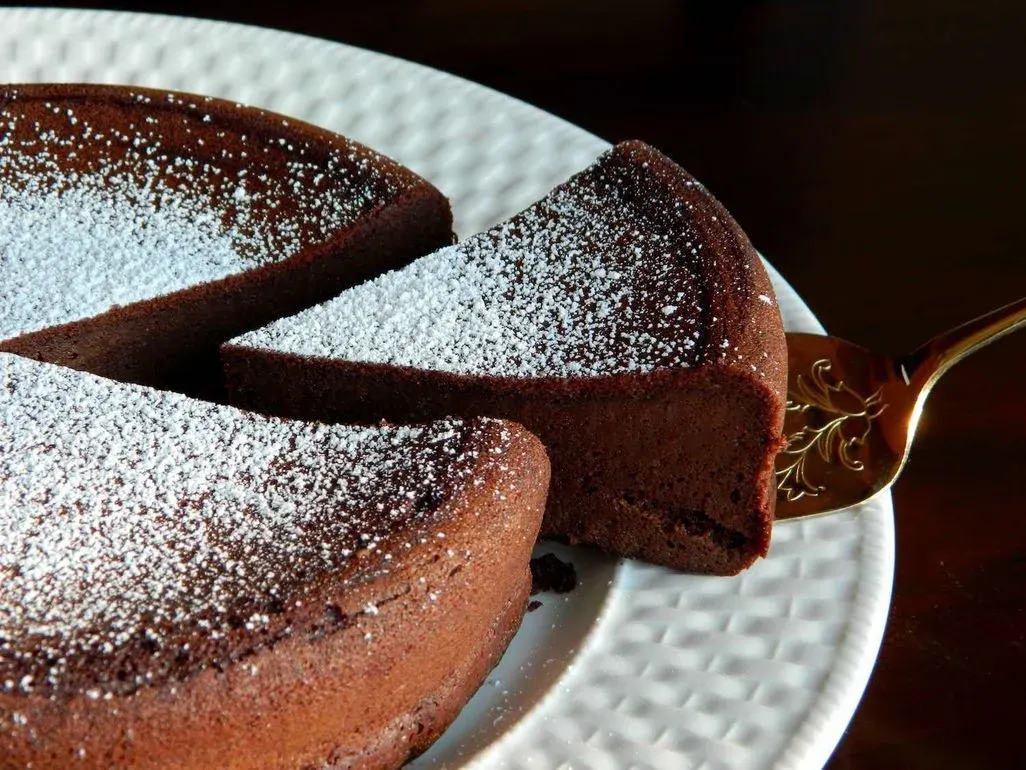 Schokoladenkuchen mit Puderzucker, ein Stück wird herausgenommen.