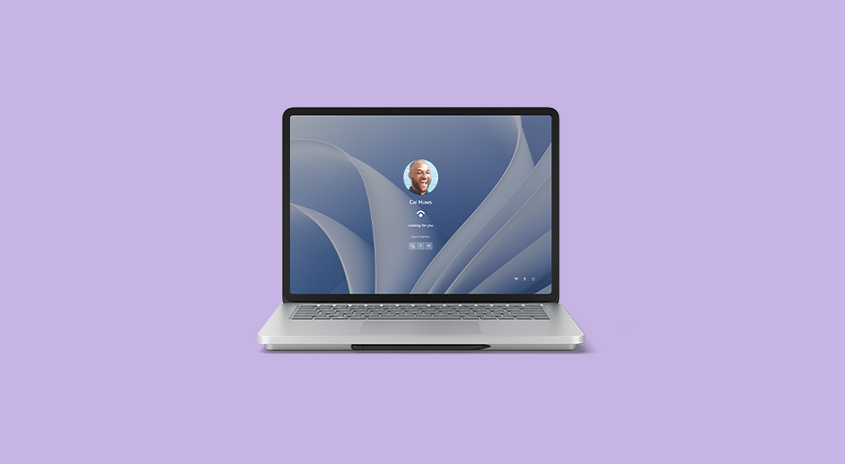 Ein Laptop mit einem Anmeldebildschirm vor einem lila Hintergrund. Der Bildschirm zeigt ein Benutzerprofil und ein Passwortfeld.