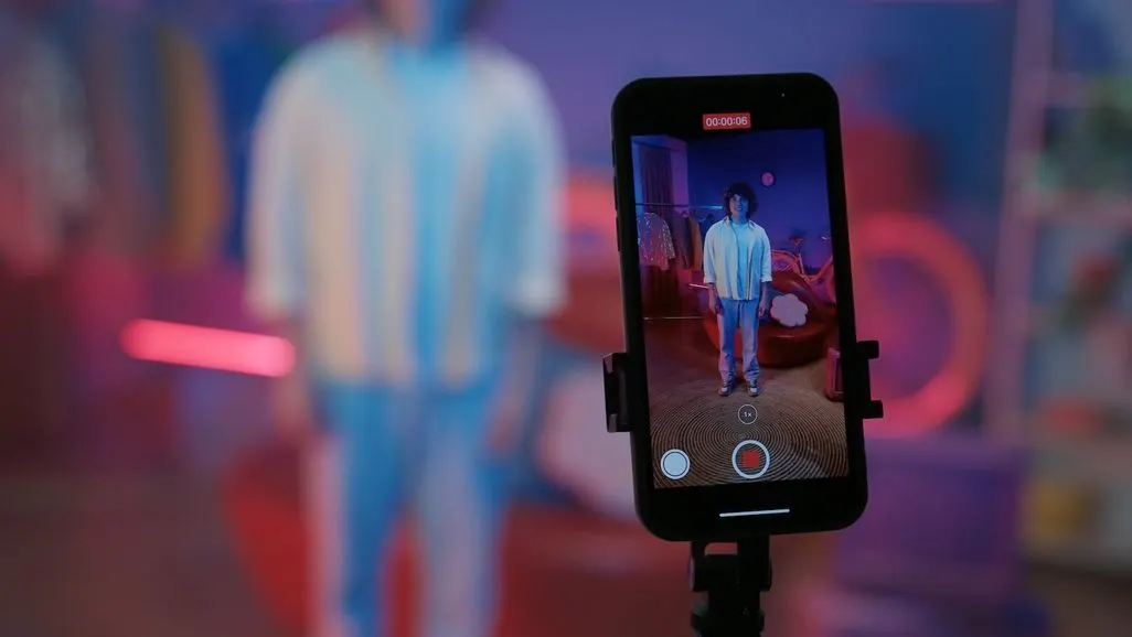 Ein Smartphone auf einem Stativ filmt eine Person in einem bunt beleuchteten Zimmer