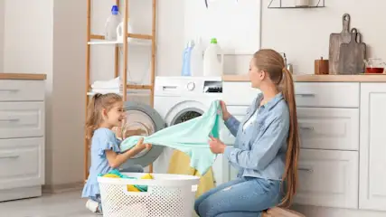Eine Frau und ein Kind sitzen vor einem Waschtrockner mit einem Korb voller Wäsche