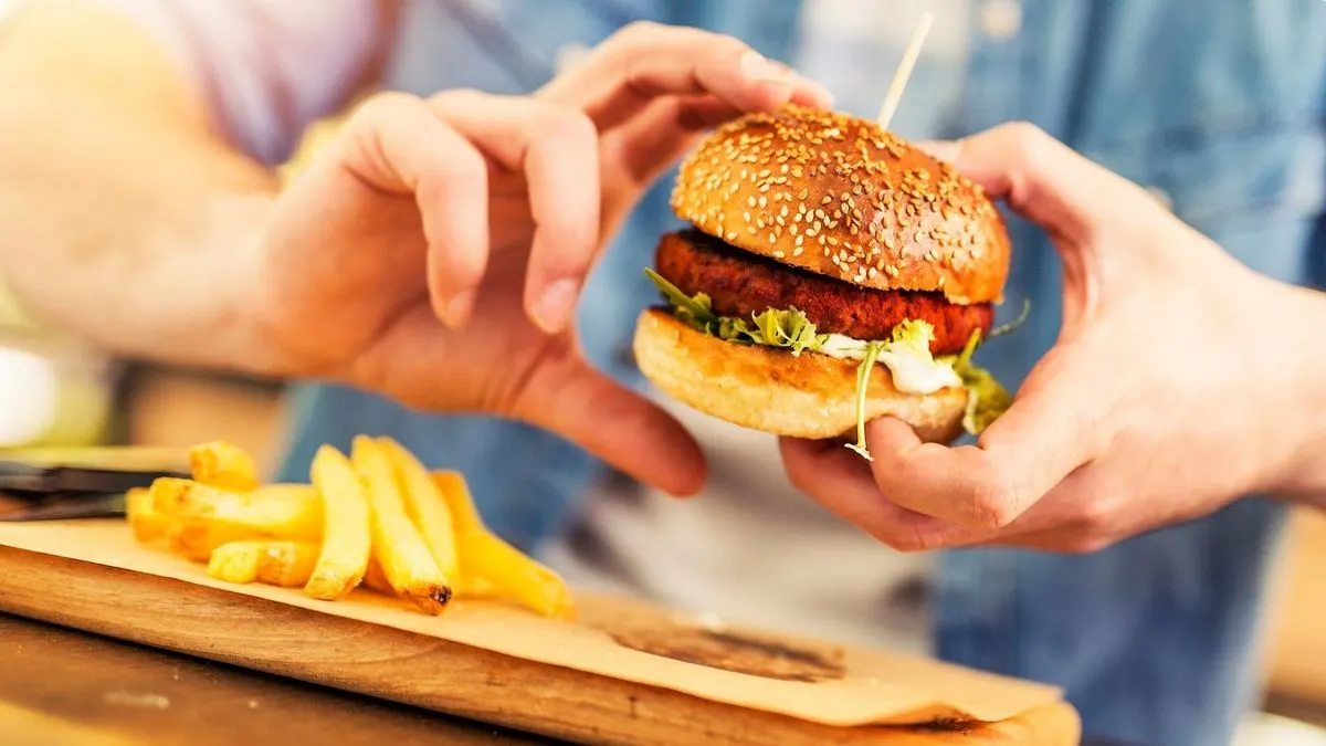 Person hält einen Burger mit Salat und Pommes auf Holzbrett.