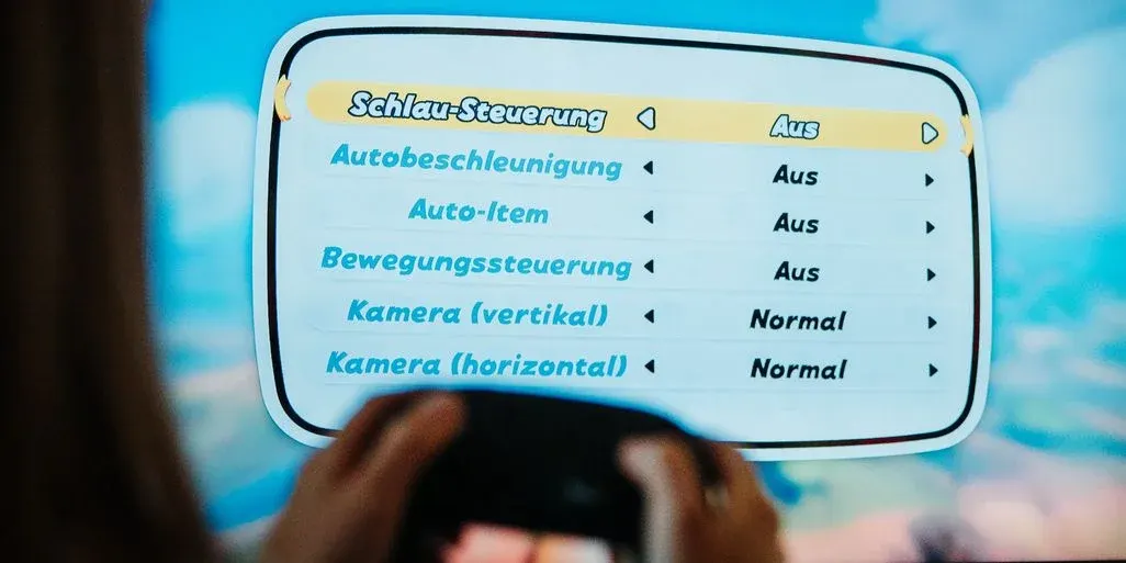 Hände halten einen schwarzen Controller vor einem blauen Bildschirm. Ein weißes Spielmenü zeigt Optionen wie "Schlau-Steuerung" und "Autobeschleunigung" auf "Aus".