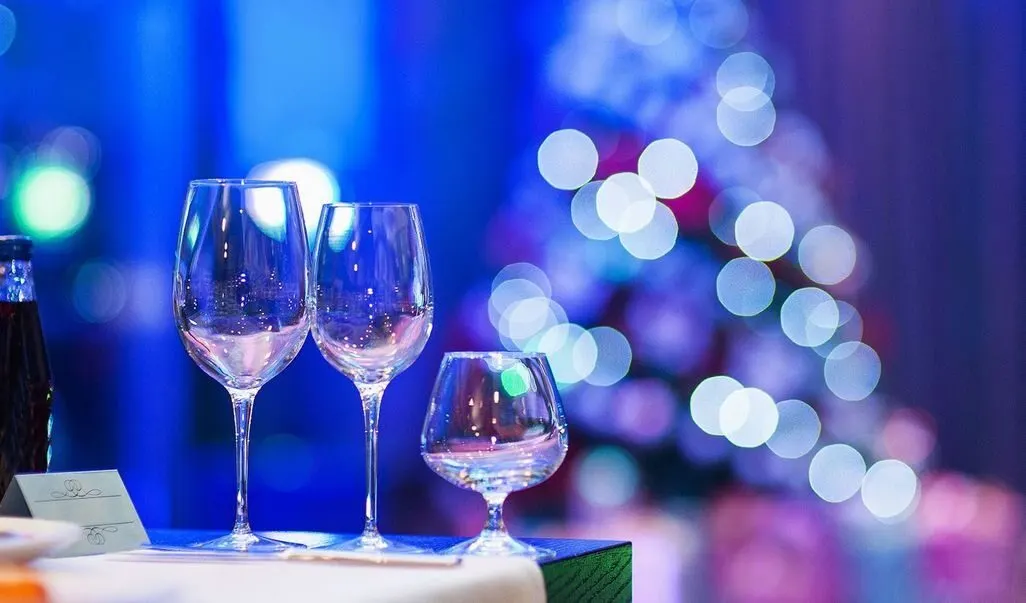 Drei leere Weinglaeser auf gedecktem Tisch mit unscharfem Weihnachtsbaum im Hintergrun