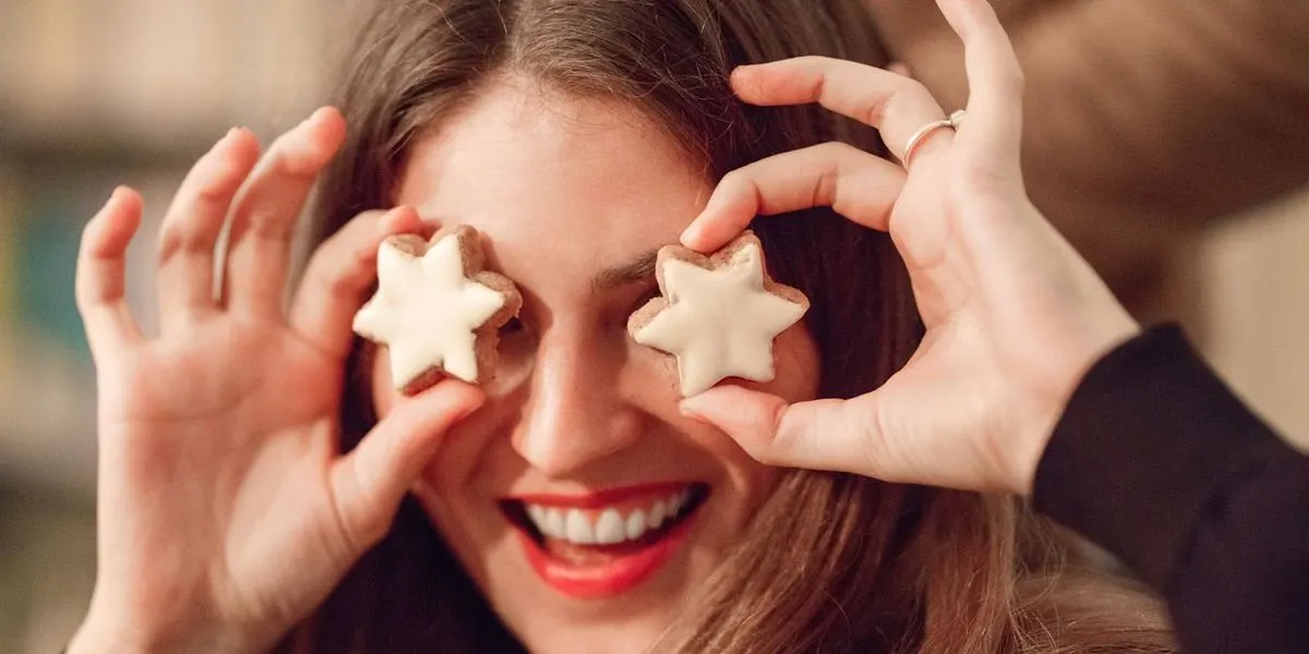 Frau hält sich lächelnd zwei sternenförmige Kekse vor die Augen.