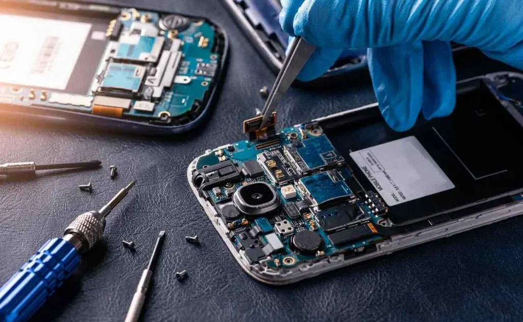 Hände in blauen Handschuhen schrauben in einem geöffneten Smartphone.
