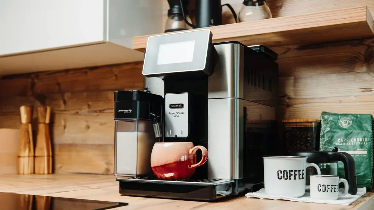DeLonghi PrimaDonnaSoul steht in einer Kueche neben Kaffeebohnen und Tassen