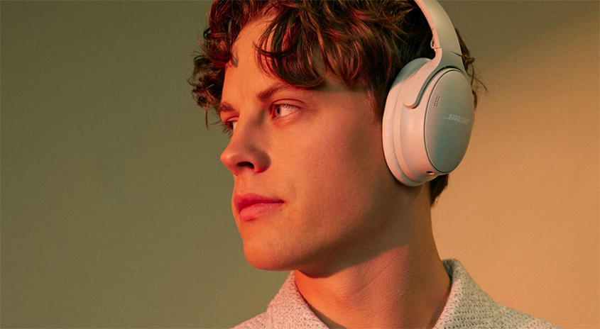 Ein junger Mann trägt weiße Kopfhörer und ein helles Hemd vor einem Hintergrund mit Farbverlauf.